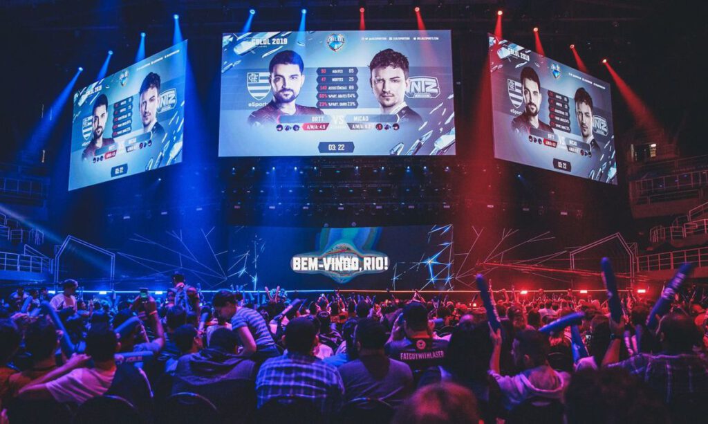 palco de edição do CBLoL, um dos principais torneios de eSports do mundo, apresentando times e jogadores em cores RGB vermelho e azul ao fundo