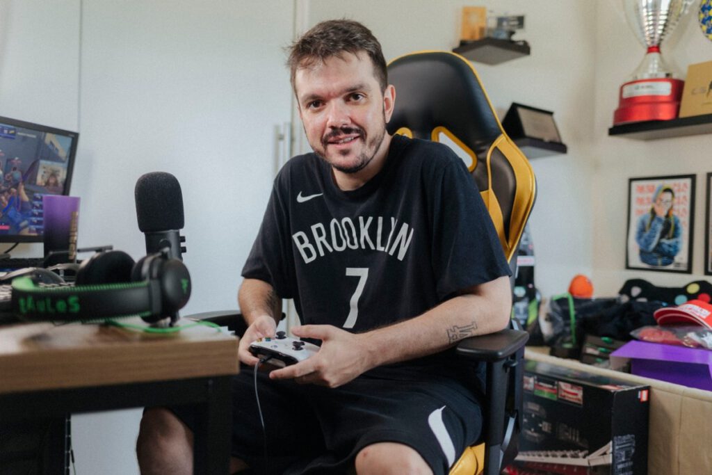 Streamer e jogador profissional de eSports Gaules sentado em cadeira gamer segurando controle de video-game