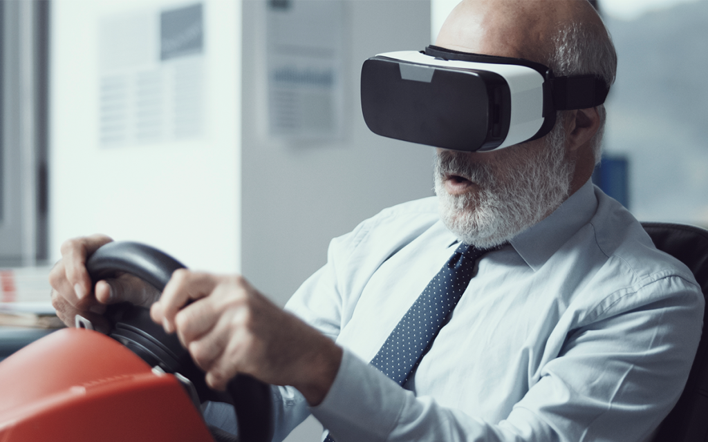 Uma pessoa com barba e cabelo brancos usando um óculos de realidade virtual segurando um console de volante representando o tema de FPS.