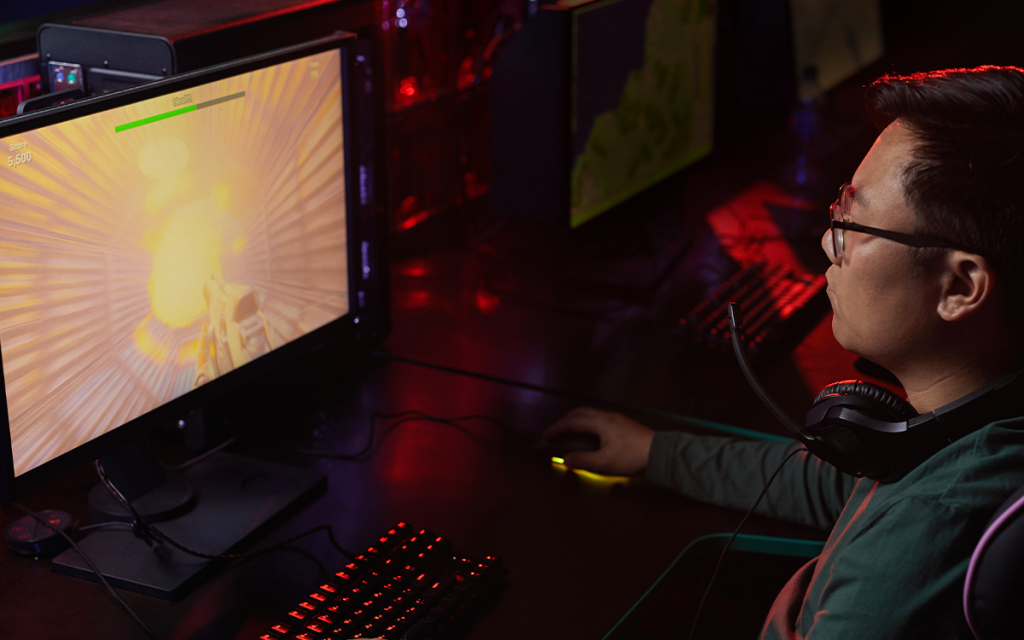 Pessoa jogando um jogo de FPS no computador com a mão no mouse e um headphone no pescoço
