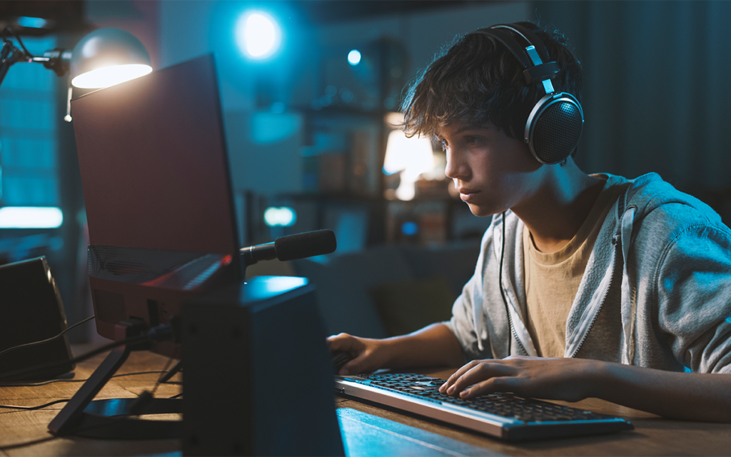 Um jovem usando fones de ouvidos com as mãos no teclado em frente ao computador representando o assunto de FPS.
