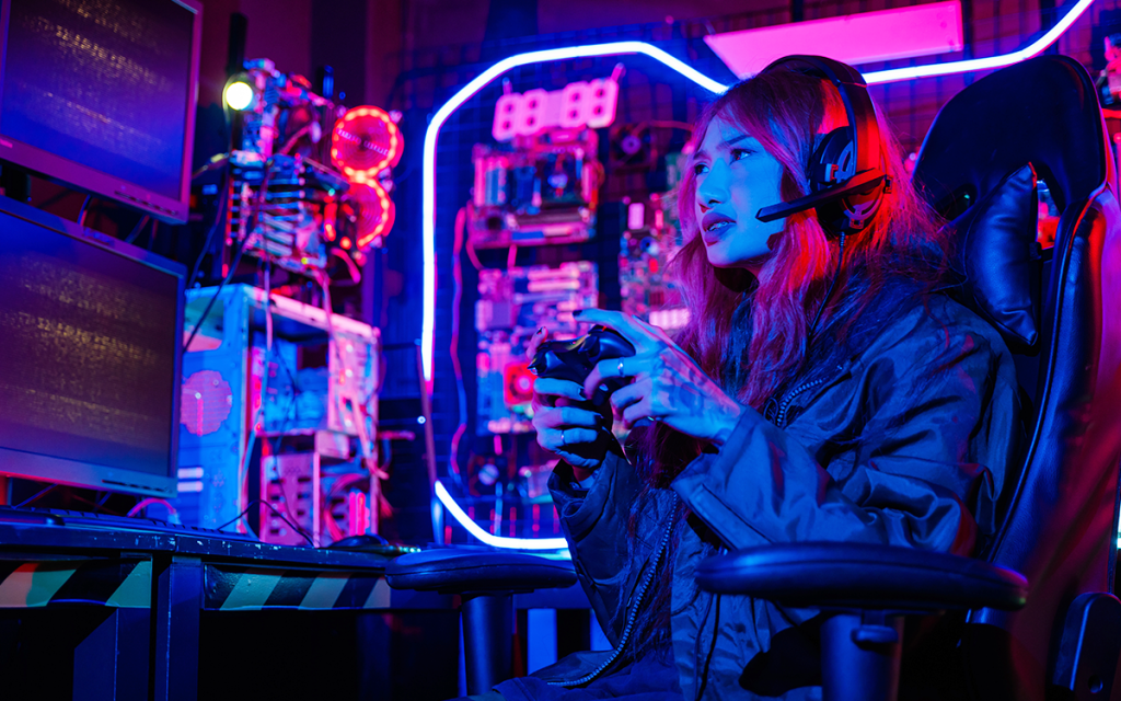 Mulher jogando videogame com headset em cadeira gamer dentro de quarto com luzes, neon e elementos tecnológicos.