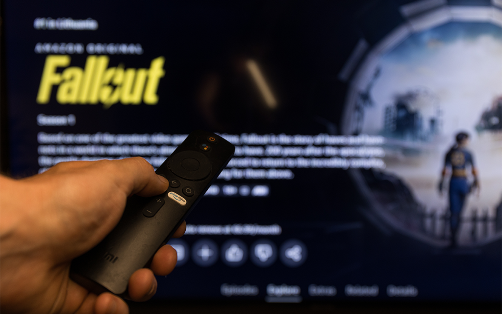 Mão de pessoa com controle em frente à televisão com a página inicial da série de Fallout no Amazon Prime, uma das séries de jogos mais populares dos últimos tempos.