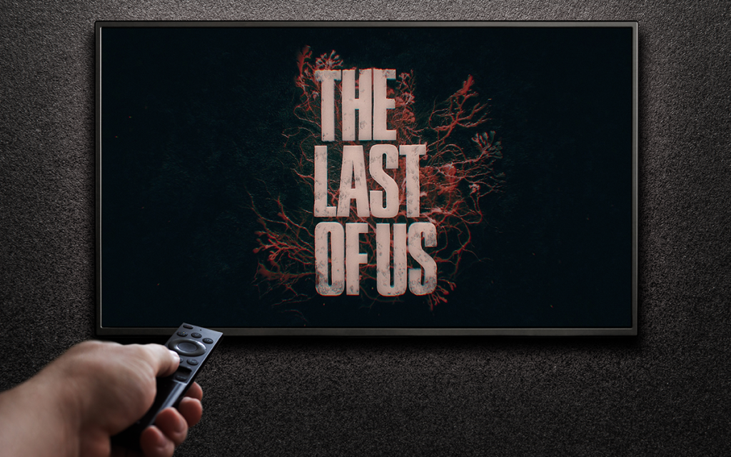 Mão com controle remoto apontando para televisor com a introdução da série The Last of Us, uma das séries de jogos de maior sucesso da história.