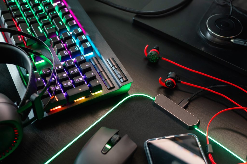 teclado gamer ao lado de mouse, headset e fones de ouvido representando os hábitos de consumo dos gamers em jogar e ouvir música ao mesmo tempo