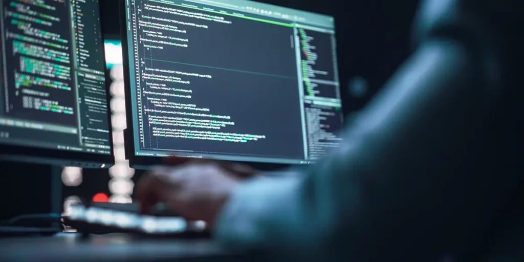 pessoa programando e trabalhando em códigos no computador em duas telas