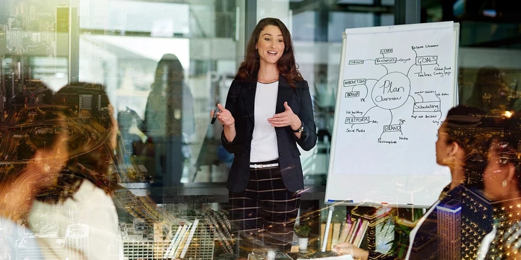 Mulher apresentando uma sessão de treinamento e desenvolvimento em um ambiente de escritório com um diagrama no quadro branco, com efeito de lente de foco seletivo destacando a apresentadora.