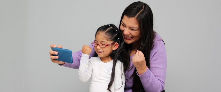 Mãe e filha felizes olhando para um smartphone, celebrando um momento juntas.