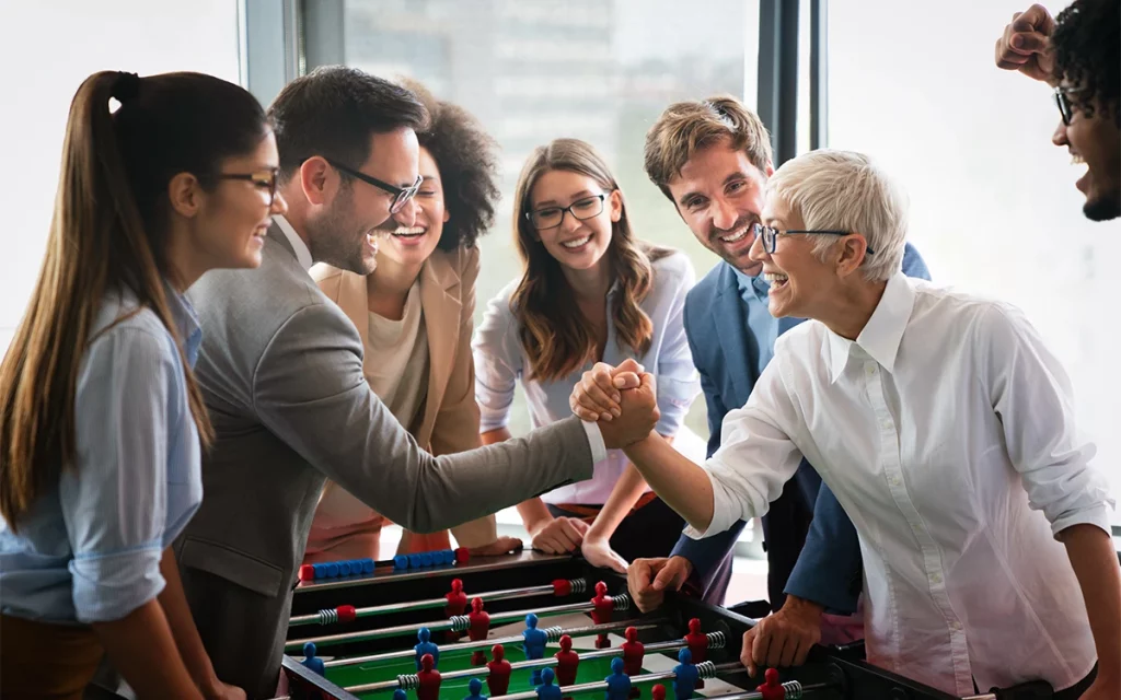 Um grupo de colegas de trabalho jogando pebolim no escritório, um exemplo de como os jogos podem ser incorporados para aumentar o engajamento e a moral da equipe.