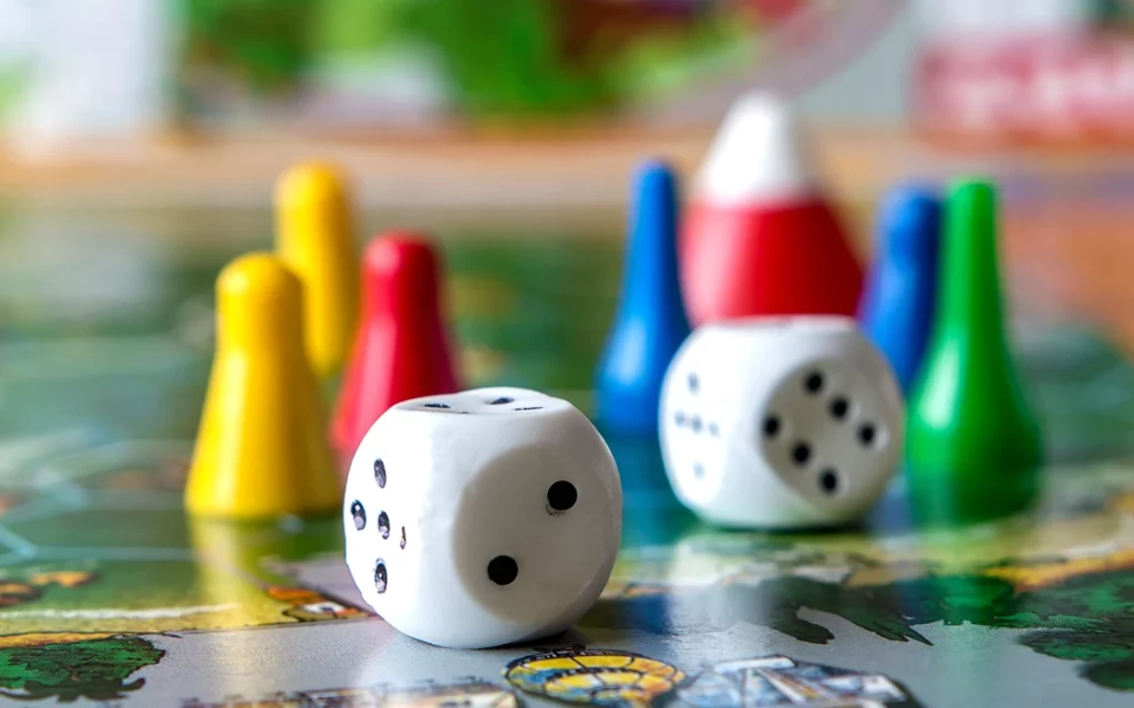 Close-up de peões coloridos e dados em um tabuleiro de jogo, elementos tradicionais em jogos de mesa que são frequentemente utilizados em estratégias de gamificação.