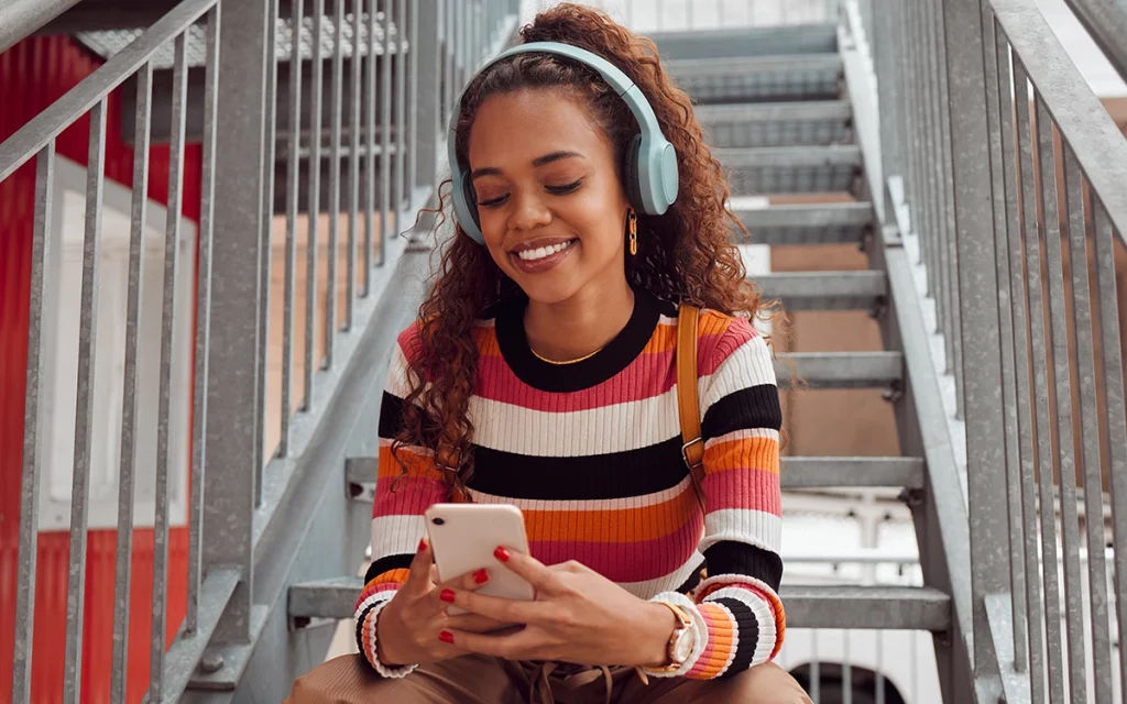 jovem sentada em escada escutando música no celular com headfone